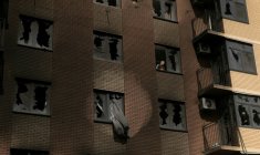 Un homme à travers une vitre brisée à l'intérieur d'un immeuble résidentiel endommagé par des frappes russes, à Kiev en Ukraine le 14 mai 2026 ( AFP / Roman PILIPEY )