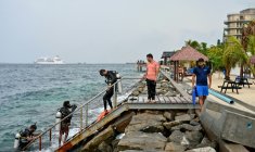 Un touriste, accompagné de guides, rentre d'une plongée en mer près de la plage de Rasfannu à Malé, le 15 mai 2026 aux Maldives ( AFP / Mohamed Afrah )
